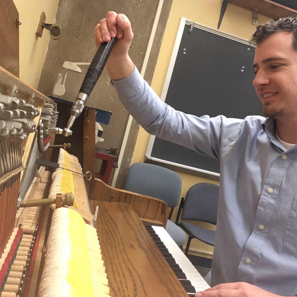 Kevin Pahl tuning an upright piano and smiling.
